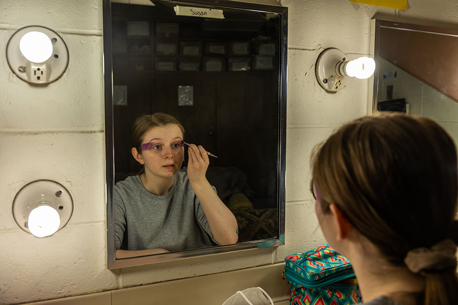 student putting on makeup in front of a mirror