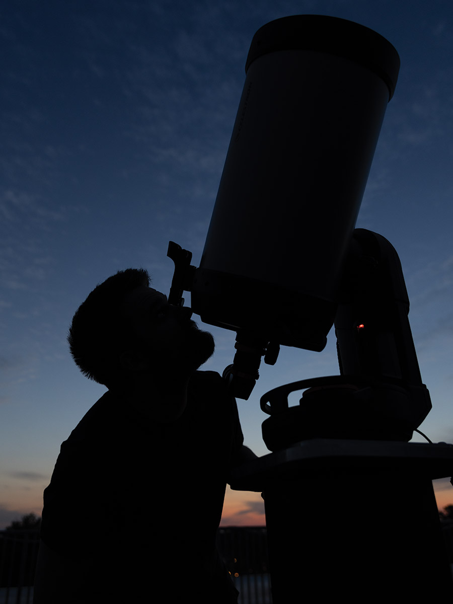 A student looks through the telescope in the observatory as the sun sets. 