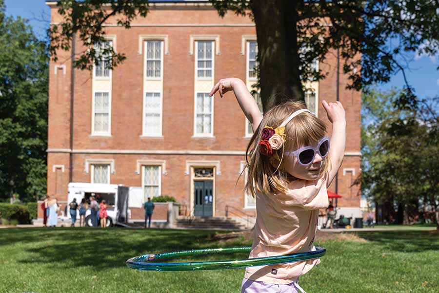 A little girl plays with a hula hoop outside of Old Main.