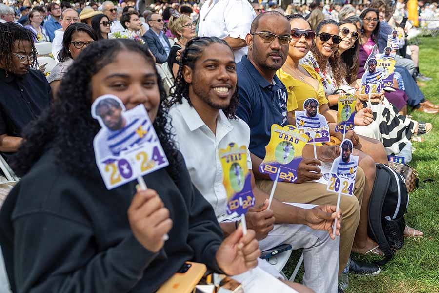 A family sits in the crowd during Commencement, holding up signs for their graduating senior.