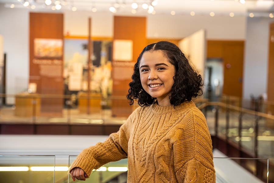 Evelyn Martinez smiles and poses with her arm on a railing inside Alumni Hall