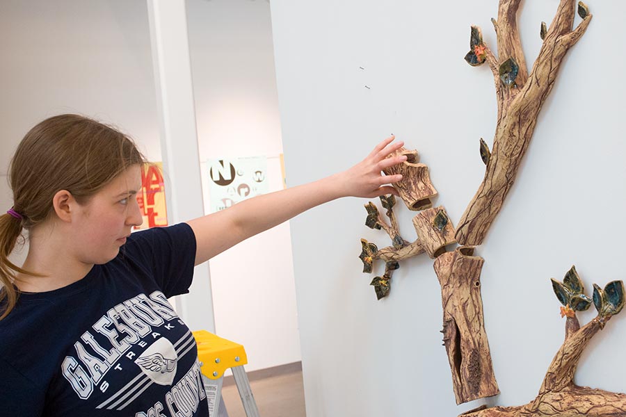 Student Lila Johnson mounts her ceramic sculpture, "Growth," on the wall for the 2018 Al Young Art Show.