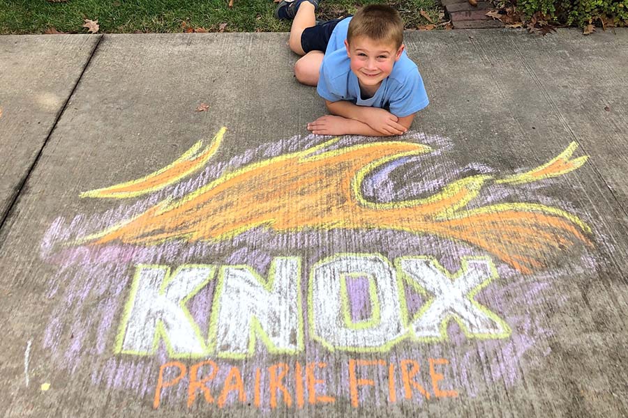 Danny Jezek-Irle lies on the sidewalk beside his chalk rendering of the Knox Prairie Fire logo.