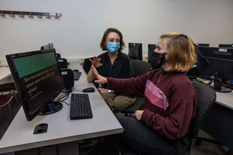 Sophia Bowley in a wine-red sweater sits in front of a computer next to Professor Foubert who wears a black blouse and listens to Sophia's question. 