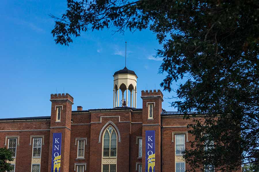 Leaves on a tree frame an exterior view of Old Main and its belltower against a blue sky