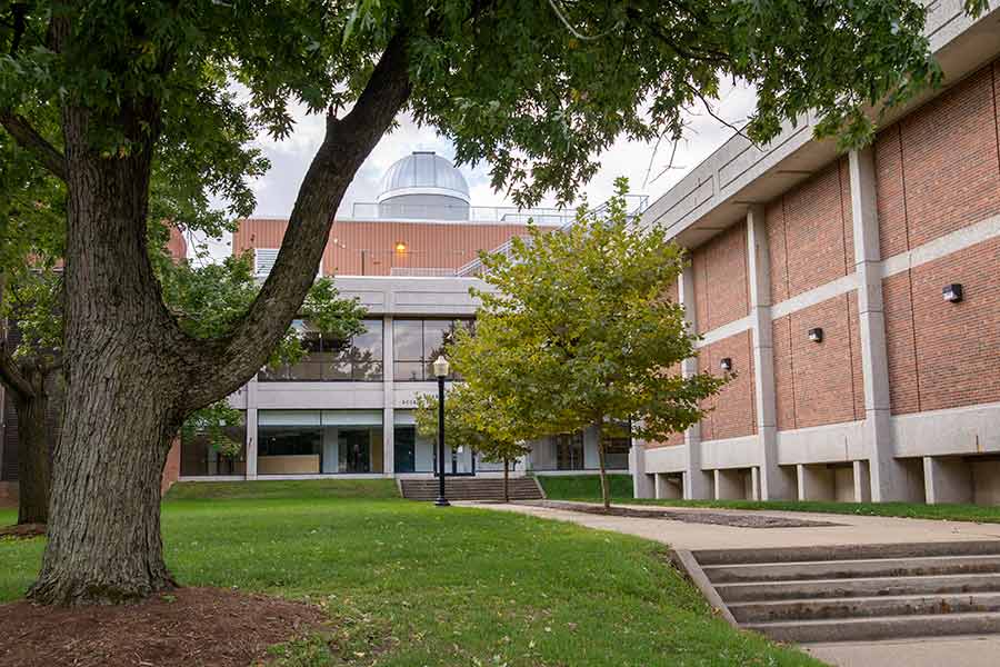 Trees and grass in front of a brick building with an astronomy observatory on the roof