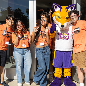 Four smiling Knox students pose with Blaze, the Prairie Fire Athletics mascot.