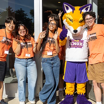 Four smiling Knox students pose with with Blaze, the Prairie Fire Athletics mascot.