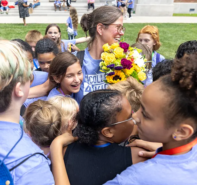 A group of Knox College four Kids students hug a teacher, who is holding a bouquet of lowers. 