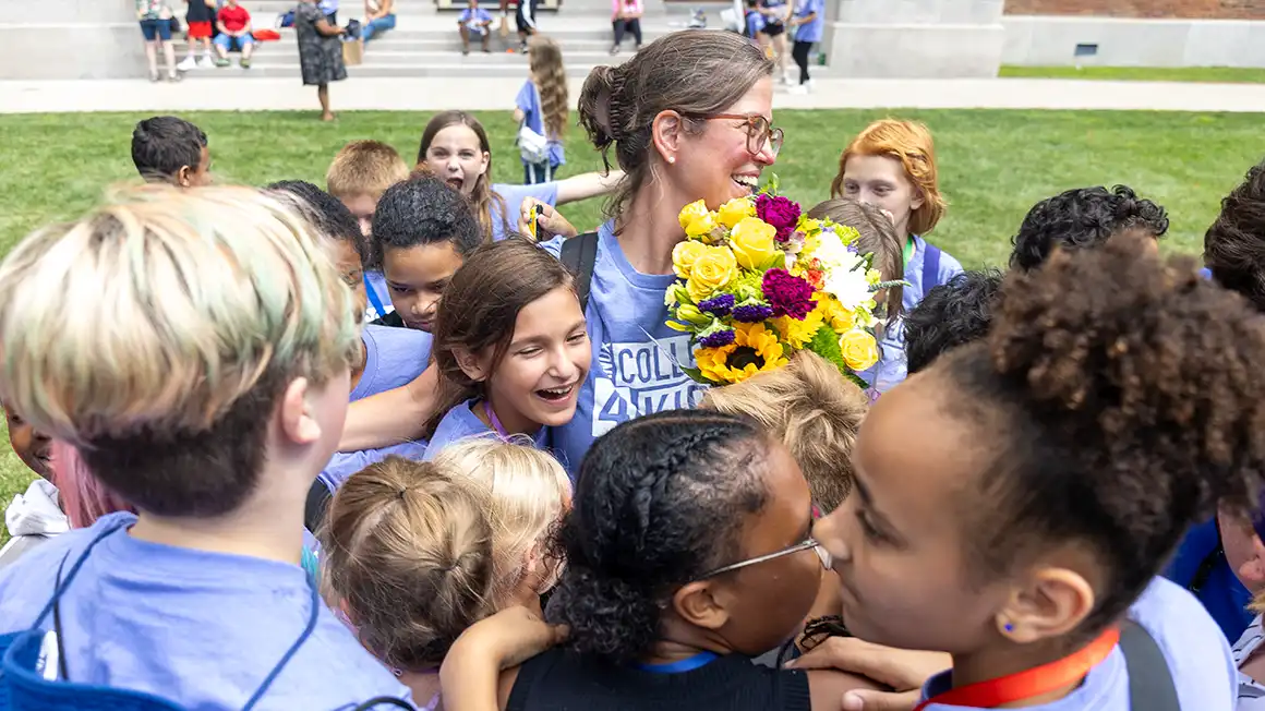 Knox College for Kids students gather around a teacher who is holding a bouquet of flowers