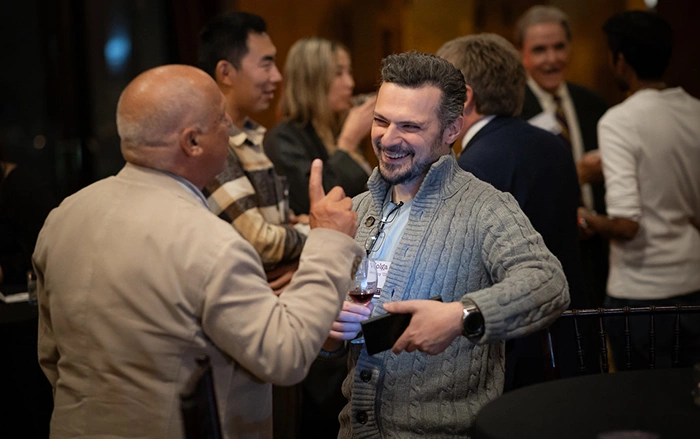 Two event attendees talk and laugh while one holds up his cell phone.