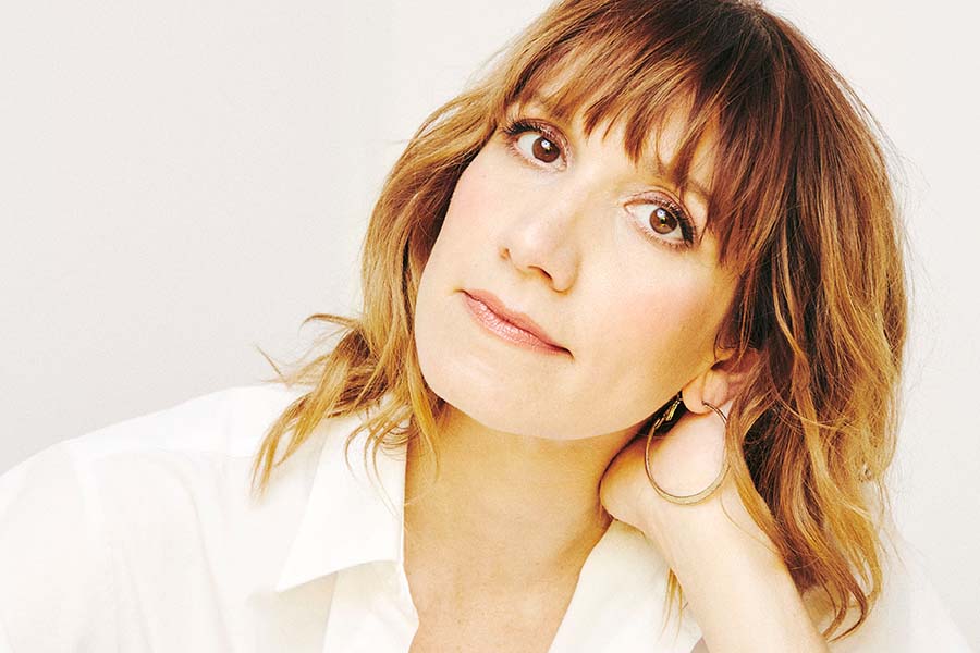 Bree Elrod in a white shirt in front of a white background. Her head is tilted and she is smiling at the camera.